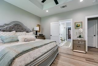 bedroom with a raised ceiling, ceiling fan, and light hardwood / wood-style flooring