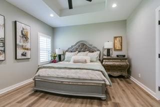 bedroom with hardwood / wood-style flooring, ceiling fan, and a raised ceiling