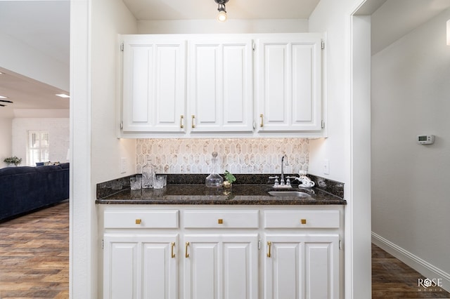 bar featuring dark hardwood / wood-style floors, tasteful backsplash, sink, dark stone countertops, and white cabinets