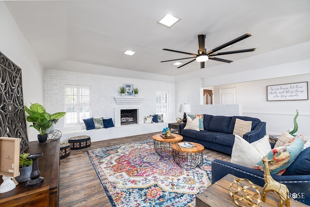 living room featuring dark wood-type flooring, lofted ceiling, ceiling fan, brick wall, and a fireplace