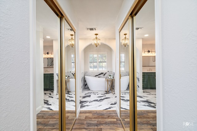 bathroom featuring an inviting chandelier, wood-type flooring, vanity, and a washtub