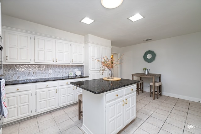 kitchen with a kitchen island, dark stone countertops, white cabinets, a kitchen breakfast bar, and light tile patterned floors