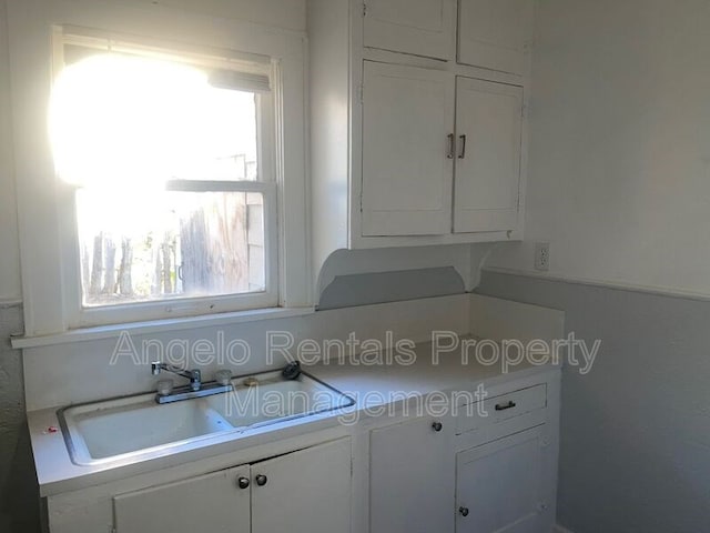 kitchen featuring light countertops, a wealth of natural light, white cabinets, and a sink