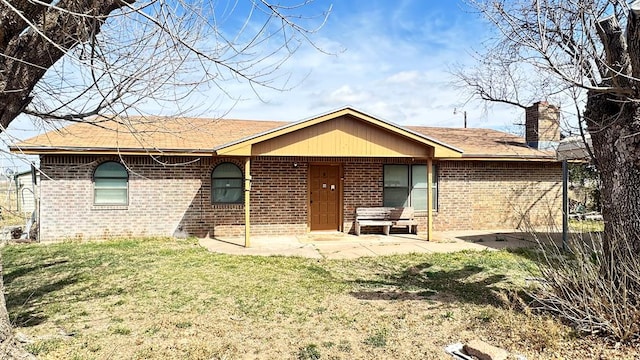 back of property with a patio area, a lawn, brick siding, and a chimney