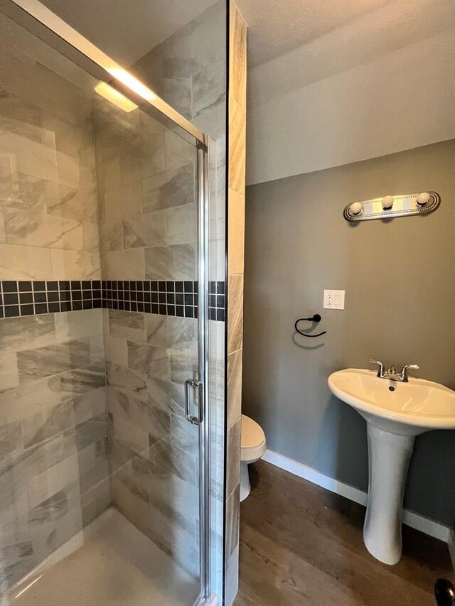 bathroom featuring toilet, a stall shower, a sink, wood finished floors, and baseboards