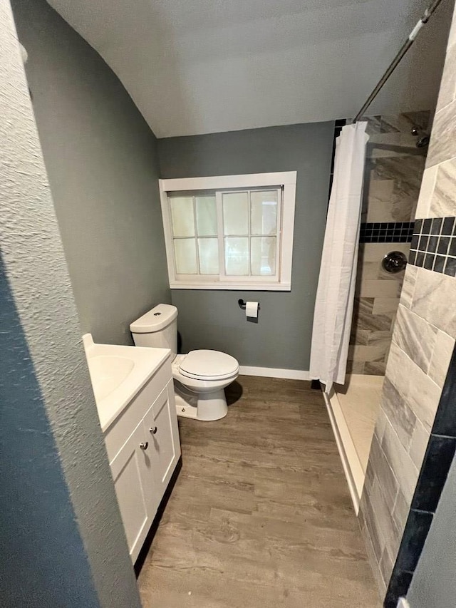 bathroom featuring toilet, wood finished floors, a tile shower, baseboards, and vanity