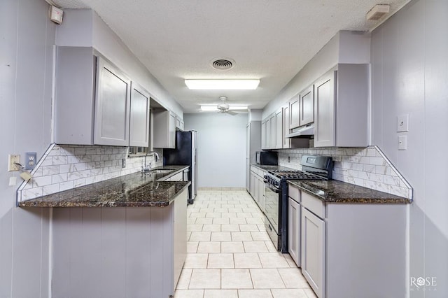 kitchen with black range with gas cooktop, sink, kitchen peninsula, dark stone counters, and backsplash