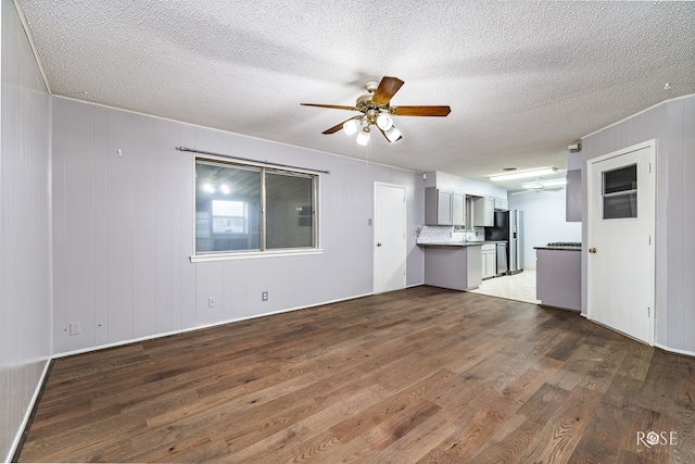 unfurnished living room with dark wood-type flooring, a textured ceiling, ceiling fan, and wood walls