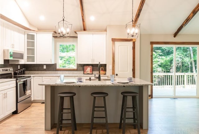 kitchen with stainless steel range oven, light hardwood / wood-style floors, white cabinets, backsplash, and a kitchen island with sink