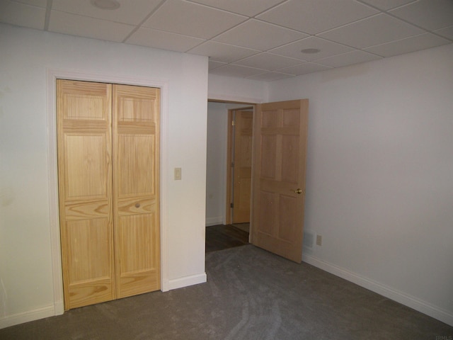 unfurnished bedroom with a closet, a drop ceiling, and dark carpet