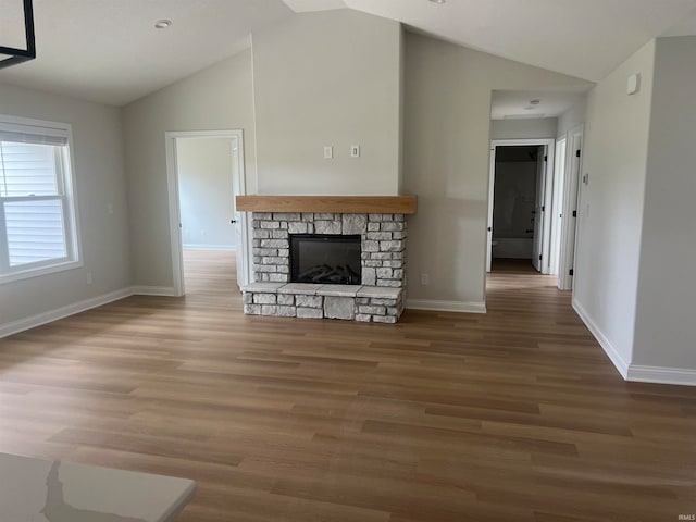 unfurnished living room featuring dark hardwood / wood-style floors, vaulted ceiling, and a stone fireplace