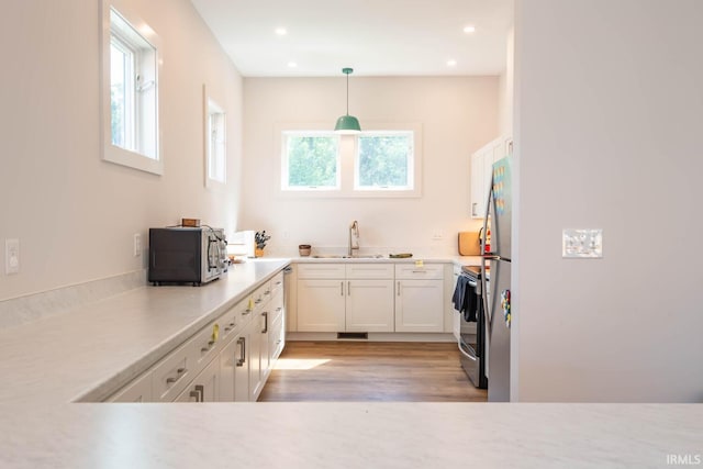 kitchen with light hardwood / wood-style flooring, hanging light fixtures, stainless steel fridge, stove, and sink