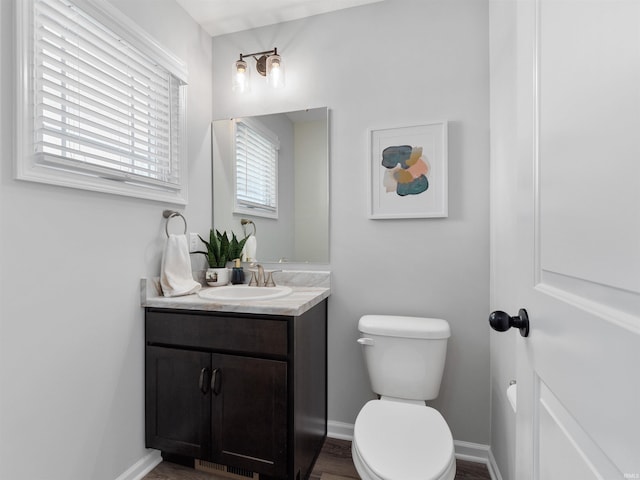 half bath with toilet, baseboards, and vanity