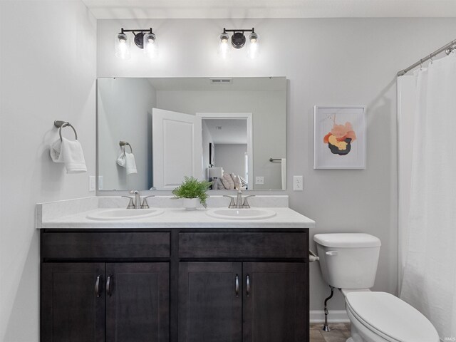 bathroom with toilet, double vanity, baseboards, and a sink