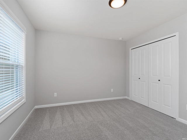 unfurnished bedroom with carpet, a closet, multiple windows, and baseboards