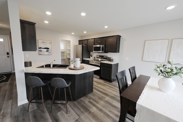 kitchen featuring a breakfast bar area, a peninsula, a sink, light countertops, and appliances with stainless steel finishes