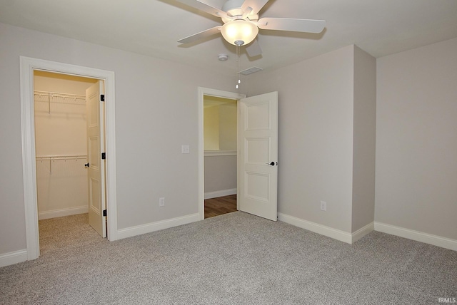 unfurnished bedroom with a closet, a walk in closet, light colored carpet, and ceiling fan
