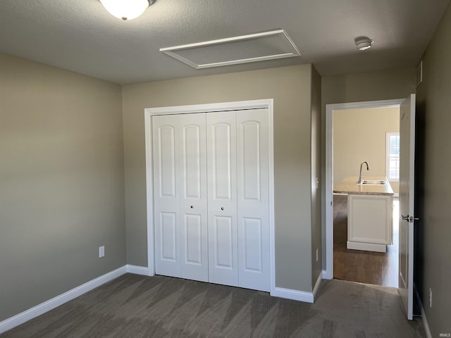 unfurnished bedroom featuring dark colored carpet, sink, a textured ceiling, and a closet