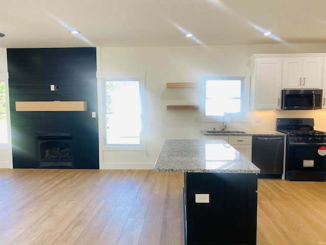 kitchen featuring light stone counters, a kitchen island, sink, black appliances, and white cabinetry