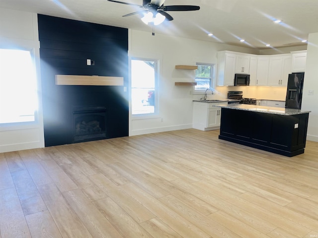 kitchen featuring gas range, a fireplace, black fridge with ice dispenser, white cabinets, and light wood-type flooring