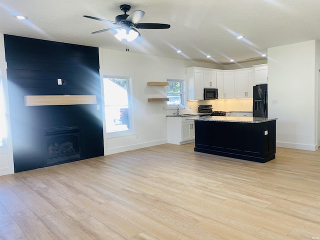 kitchen with black appliances, sink, light wood-type flooring, a kitchen island, and white cabinetry