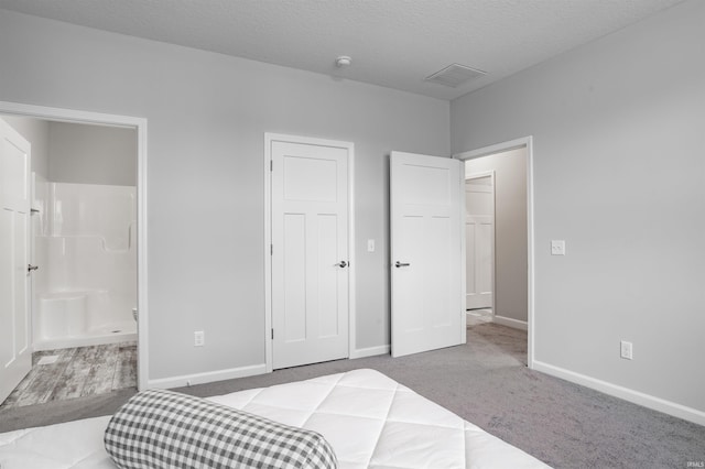 carpeted bedroom with ensuite bathroom and a textured ceiling