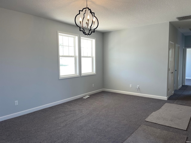 empty room featuring a textured ceiling, dark carpet, and a notable chandelier