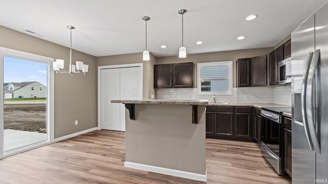 kitchen with a center island, stainless steel appliances, light hardwood / wood-style flooring, pendant lighting, and a kitchen bar