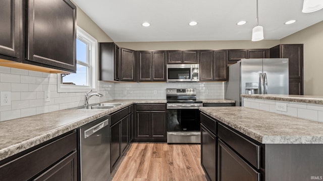 kitchen with appliances with stainless steel finishes, light wood-type flooring, backsplash, sink, and hanging light fixtures