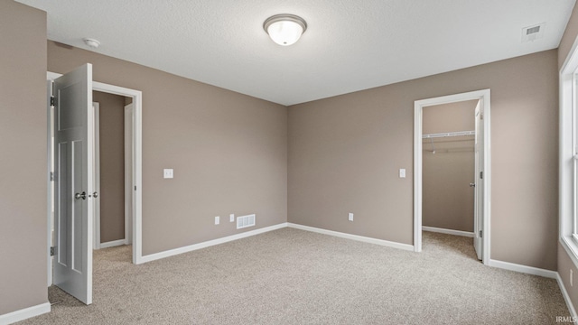 unfurnished bedroom with light carpet, a textured ceiling, a walk in closet, and a closet