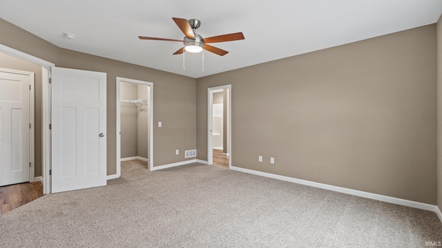 unfurnished bedroom featuring carpet, a walk in closet, a closet, and ceiling fan