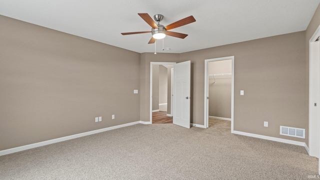 unfurnished bedroom featuring a closet, a spacious closet, ceiling fan, and light colored carpet