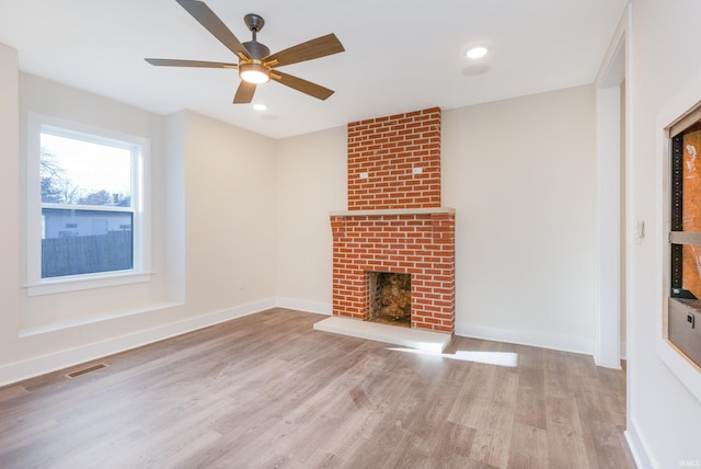 unfurnished living room with ceiling fan, a brick fireplace, and light hardwood / wood-style flooring