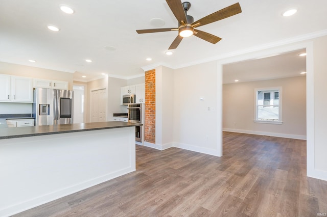 kitchen featuring appliances with stainless steel finishes, white cabinetry, wood-type flooring, ornamental molding, and ceiling fan