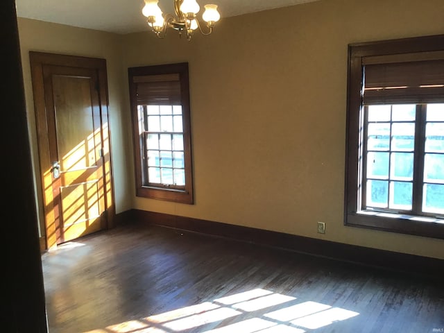 spare room featuring an inviting chandelier, a wealth of natural light, and dark wood-type flooring