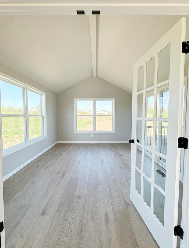 empty room featuring vaulted ceiling with beams, a wealth of natural light, and light wood-type flooring