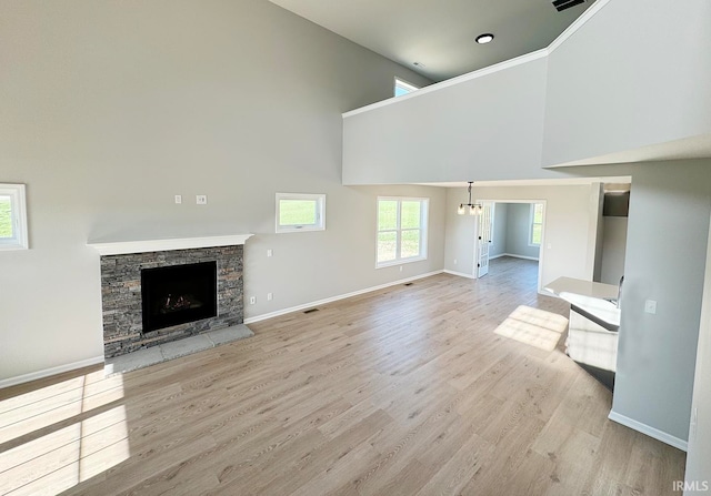 unfurnished living room featuring a high ceiling, a chandelier, a fireplace, and light hardwood / wood-style flooring