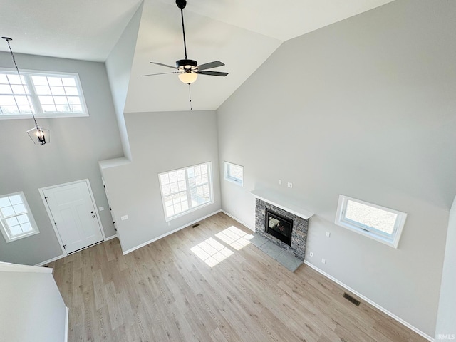 unfurnished living room with ceiling fan, a stone fireplace, high vaulted ceiling, and light hardwood / wood-style flooring