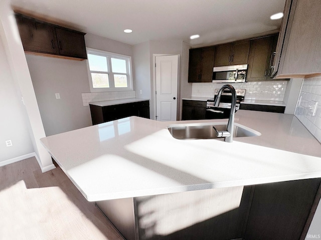 kitchen with sink, range with electric cooktop, a kitchen bar, decorative backsplash, and light wood-type flooring