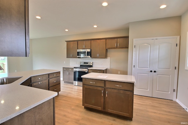 kitchen with backsplash, sink, a center island, light wood-type flooring, and appliances with stainless steel finishes