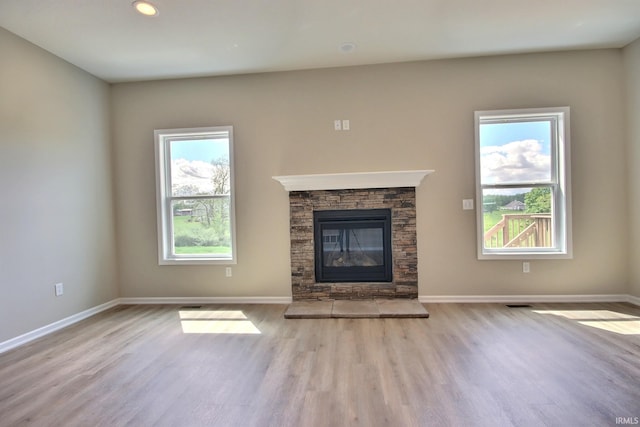 unfurnished living room featuring light hardwood / wood-style floors and a stone fireplace