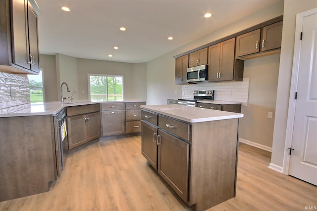 kitchen featuring stainless steel appliances, sink, light wood-type flooring, and a kitchen island