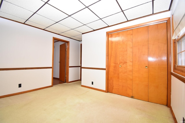 unfurnished bedroom featuring light carpet, a closet, and a drop ceiling