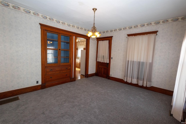 carpeted empty room with a notable chandelier