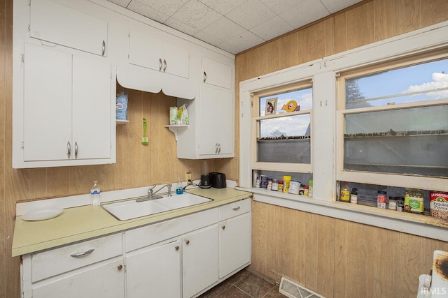 kitchen featuring wooden walls, white cabinetry, and sink