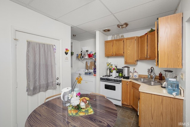 kitchen with white gas stove, sink, dark tile floors, a paneled ceiling, and washer and dryer