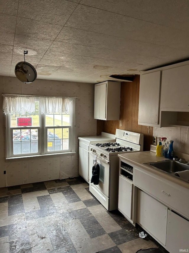 kitchen featuring white gas range oven, sink, dark tile floors, and white cabinetry