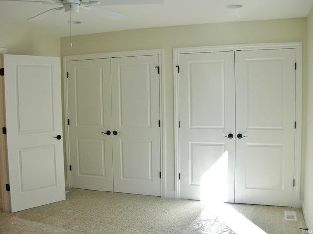 unfurnished bedroom featuring multiple closets, ceiling fan, and light colored carpet