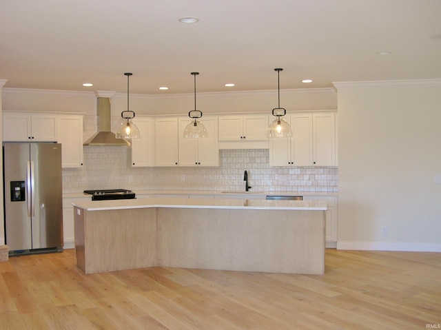 kitchen with stainless steel fridge, a kitchen island, hanging light fixtures, and wall chimney exhaust hood