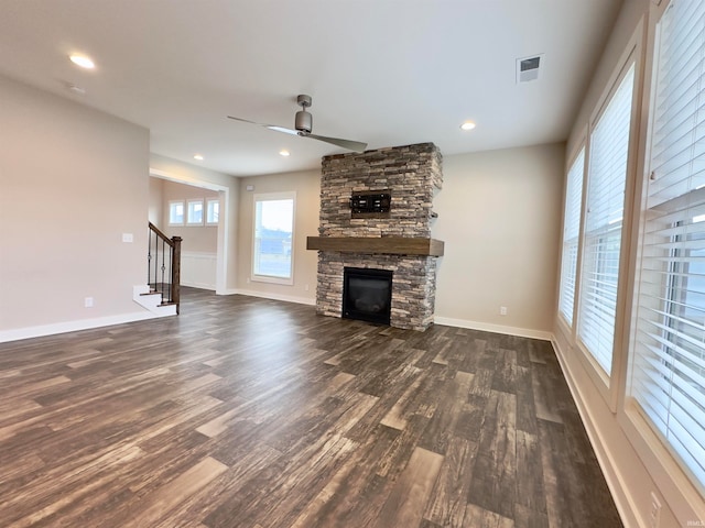 unfurnished living room with dark hardwood / wood-style flooring, ceiling fan, and a stone fireplace